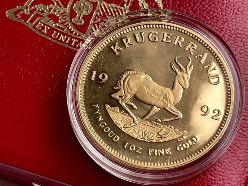 1992 1oz fine gold Krugerrand coin displayed on a vibrant red passport background, highlighting its rich colour and historical significance.