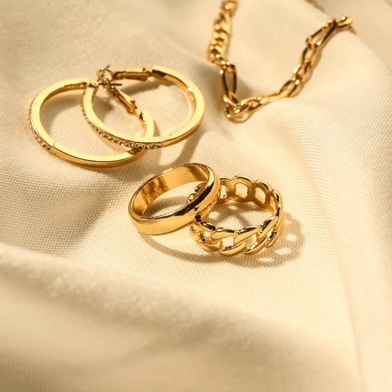 Display of gold diamond hoop earrings, a plain gold band ring, a chain-design gold ring, and a matching gold chain necklace.