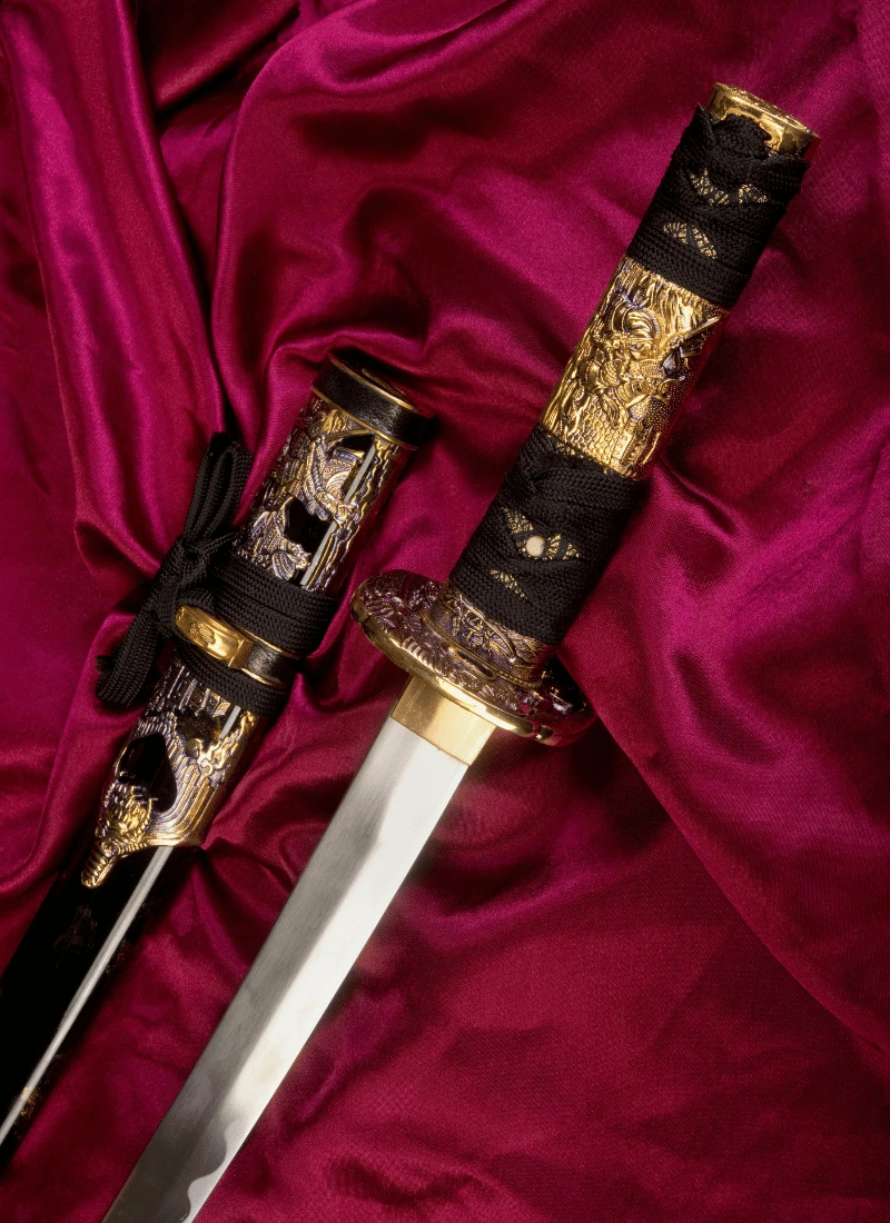 Two antique swords with gold and rope handles, one sheathed and the other displaying its sharp blade, set against a rich red velvet background.
